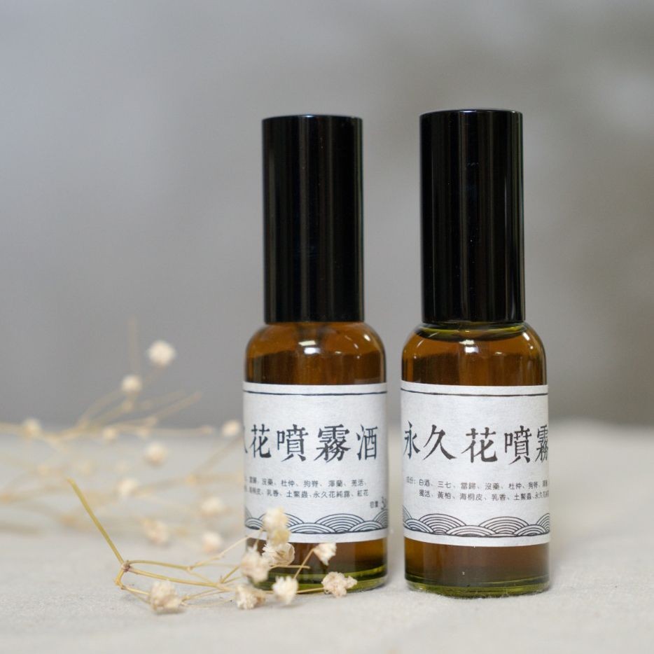 Two brown glass spray bottles with white labels and black caps, with dried flowers in the background.