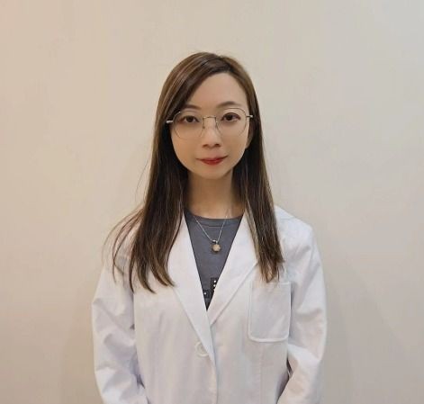 Woman in a white lab coat standing against a plain background.