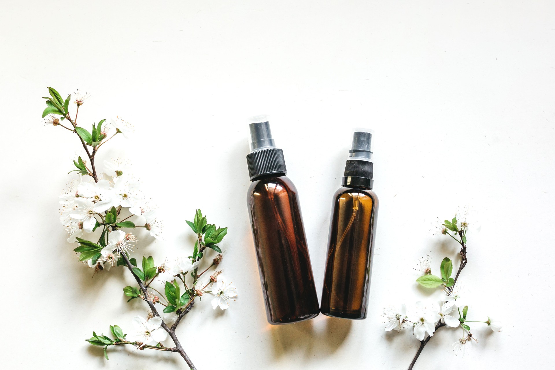 Cosmetic bottles made of dark amber glass on a white background with flowering branches of cherry or apple trees.The concept of natural cosmetics